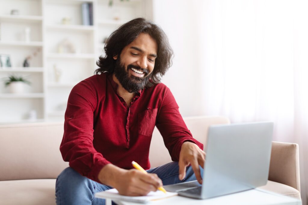 Positive eastern guy attending webinar, using laptop at home